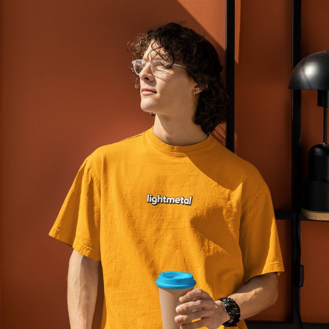 Wild Yellow - Person wearing a yellow 'lightmetal' t-shirt holding a blue cup against an orange wall.