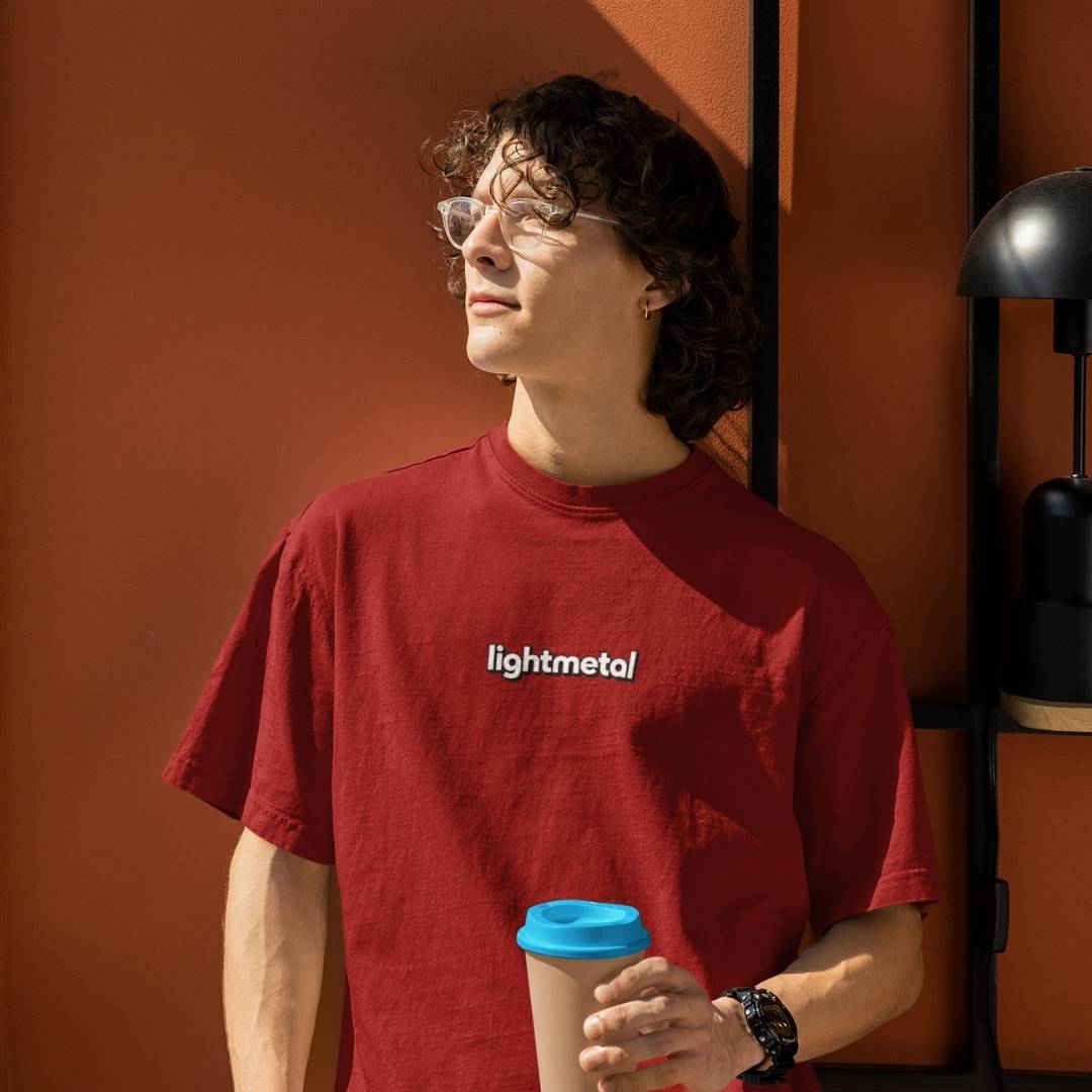 Primal Red - Person wearing a red 'lightmetal' t-shirt holding a coffee cup against an orange wall.