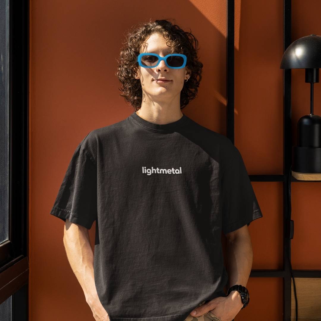 Honest Black - Person wearing an honest black t-shirt with 'lightmetal' text, standing against an orange wall.