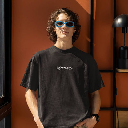 Honest Black - Person wearing an honest black t-shirt with 'lightmetal' text, standing against an orange wall.