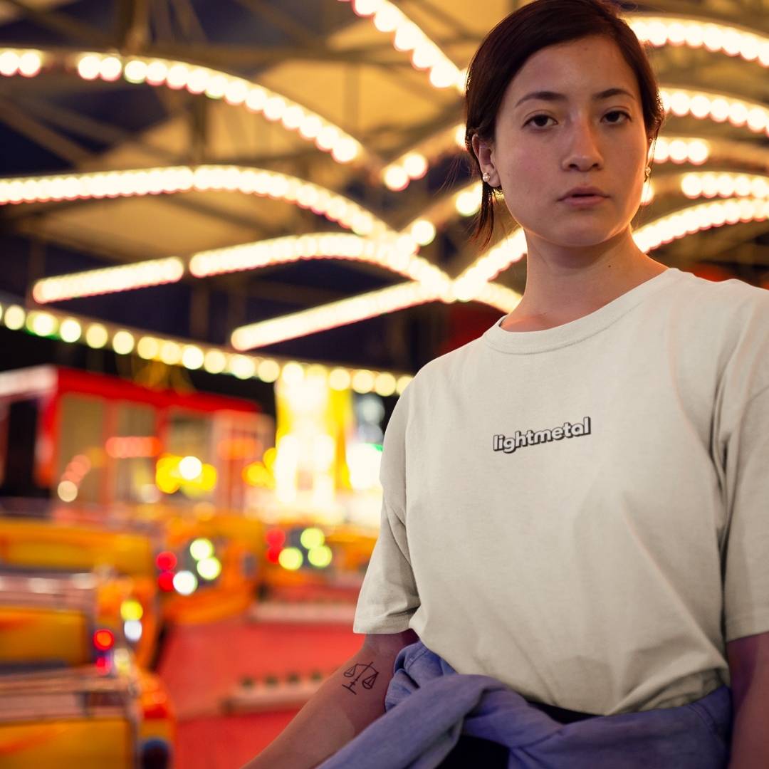 Corporate Beige - Person wearing a beige t-shirt with 'Rightmetal' logo in a colorful, blurred indoor setting