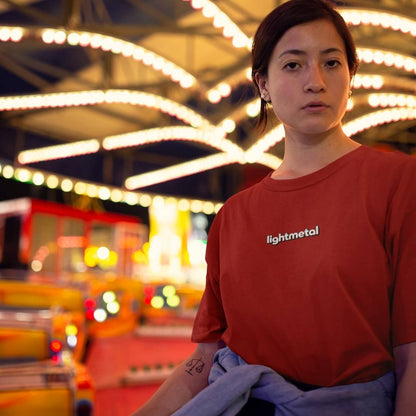 Primal Red - Person wearing a red 'lightmetal' shirt in a festive setting with lights and blurred rides.