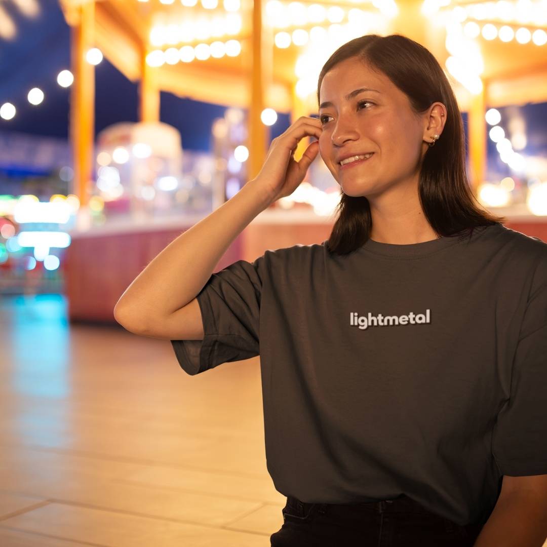 Honest Black - Woman wearing a 'lightmetal' shirt in an outdoor setting with blurred lights in the background