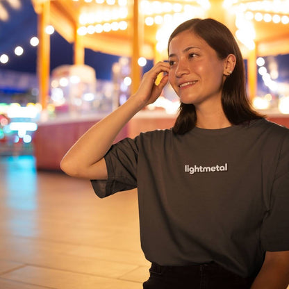 Honest Black - Woman wearing a 'lightmetal' shirt in an outdoor setting with blurred lights in the background