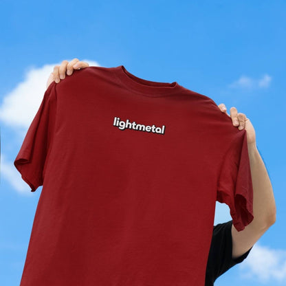 Primal Red - t-shirt with 'lightmetal' logo held up against a blue sky.