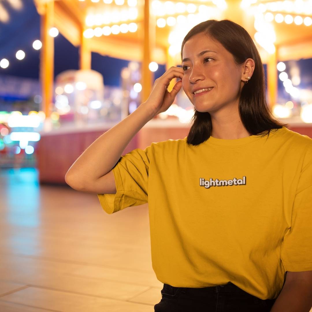 Wild Yellow - Woman wearing a yellow 'lightmetal' shirt in an outdoor setting with blurred lights in the background
