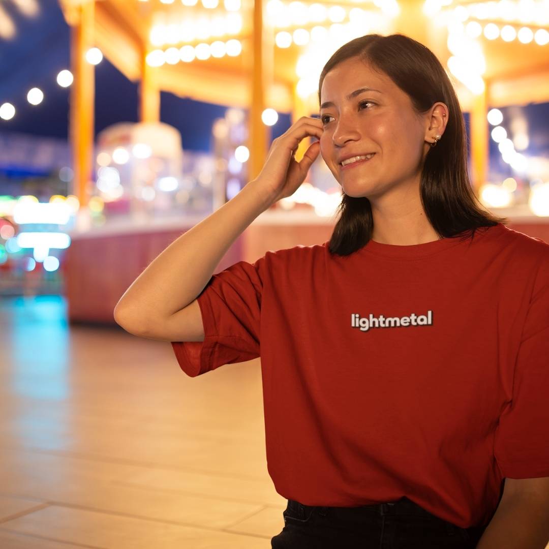 Primal Red - Person wearing a red 'lightmetal' shirt in an outdoor setting with blurred lights in the background