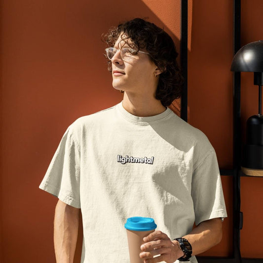Corporate Beige - Person wearing a light-colored t-shirt with 'lightmetal' text, holding a coffee cup with a blue lid against an orange wall.