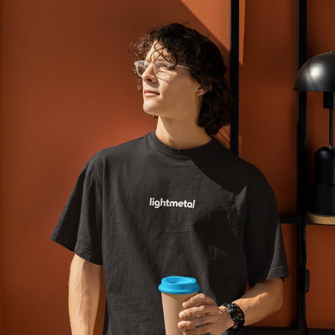 Honest Black - Person wearing a black 'lightmetal' t-shirt holding a coffee cup against an orange wall.